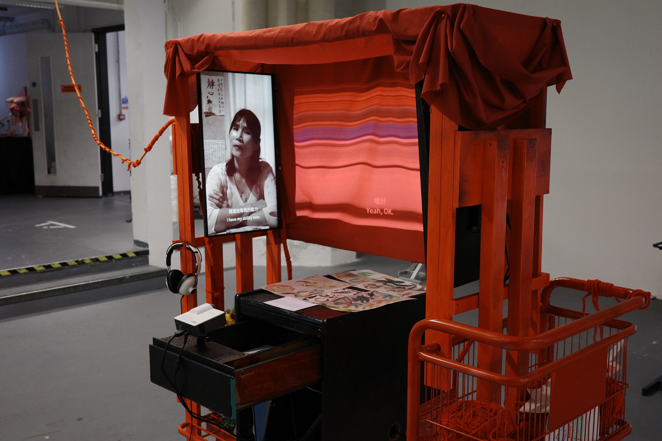 Spatial view of the red pushable cart installation with video, projection, and surrounding objects